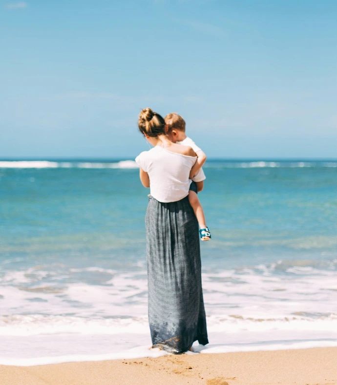 woman carrying toddler on seashore